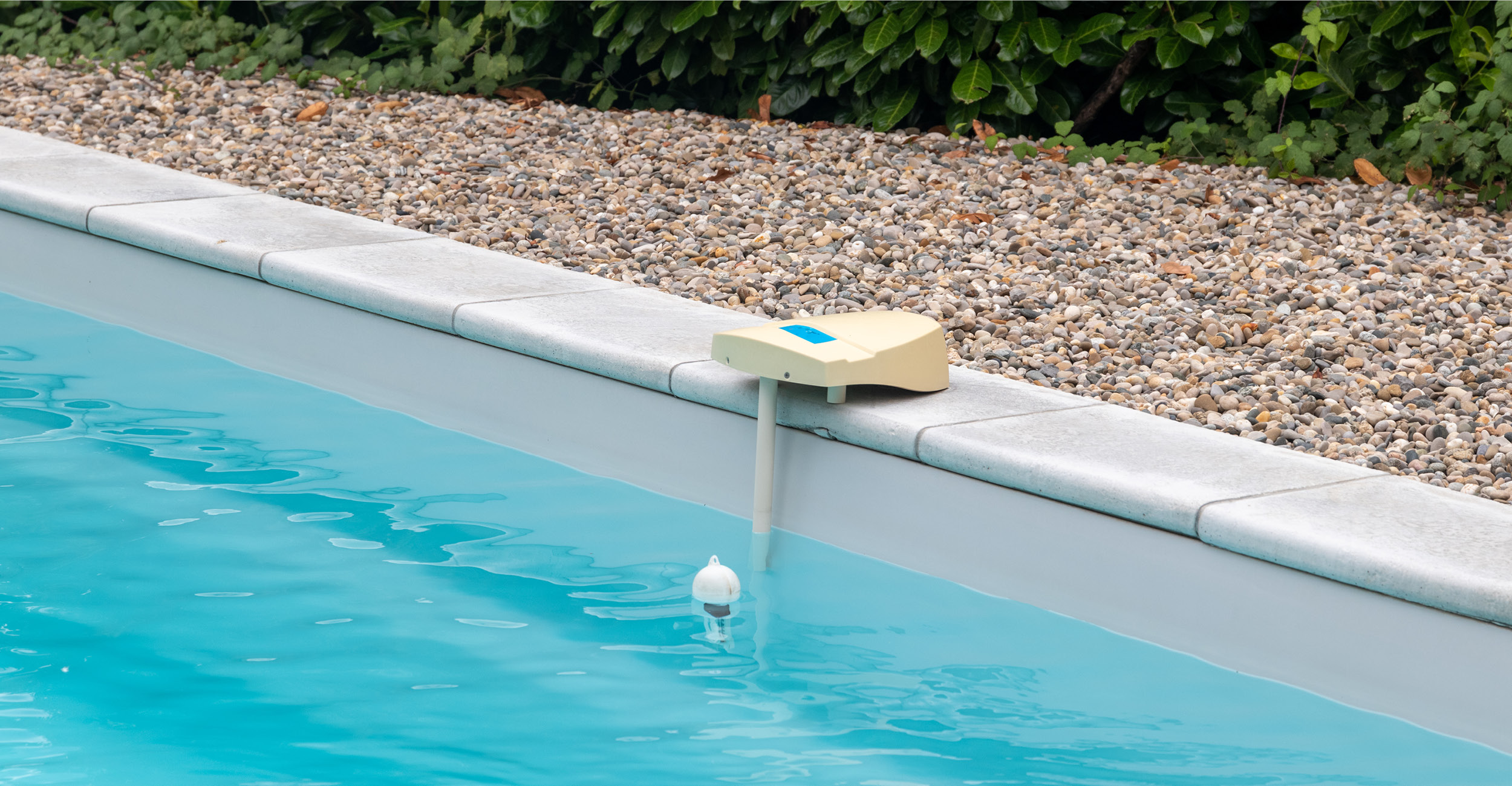 Piscine coque avec eau bleue claire, dispositif de régulation beige au bord pour contrôle du niveau, entourée de carrelage esthétique et végétation soignée