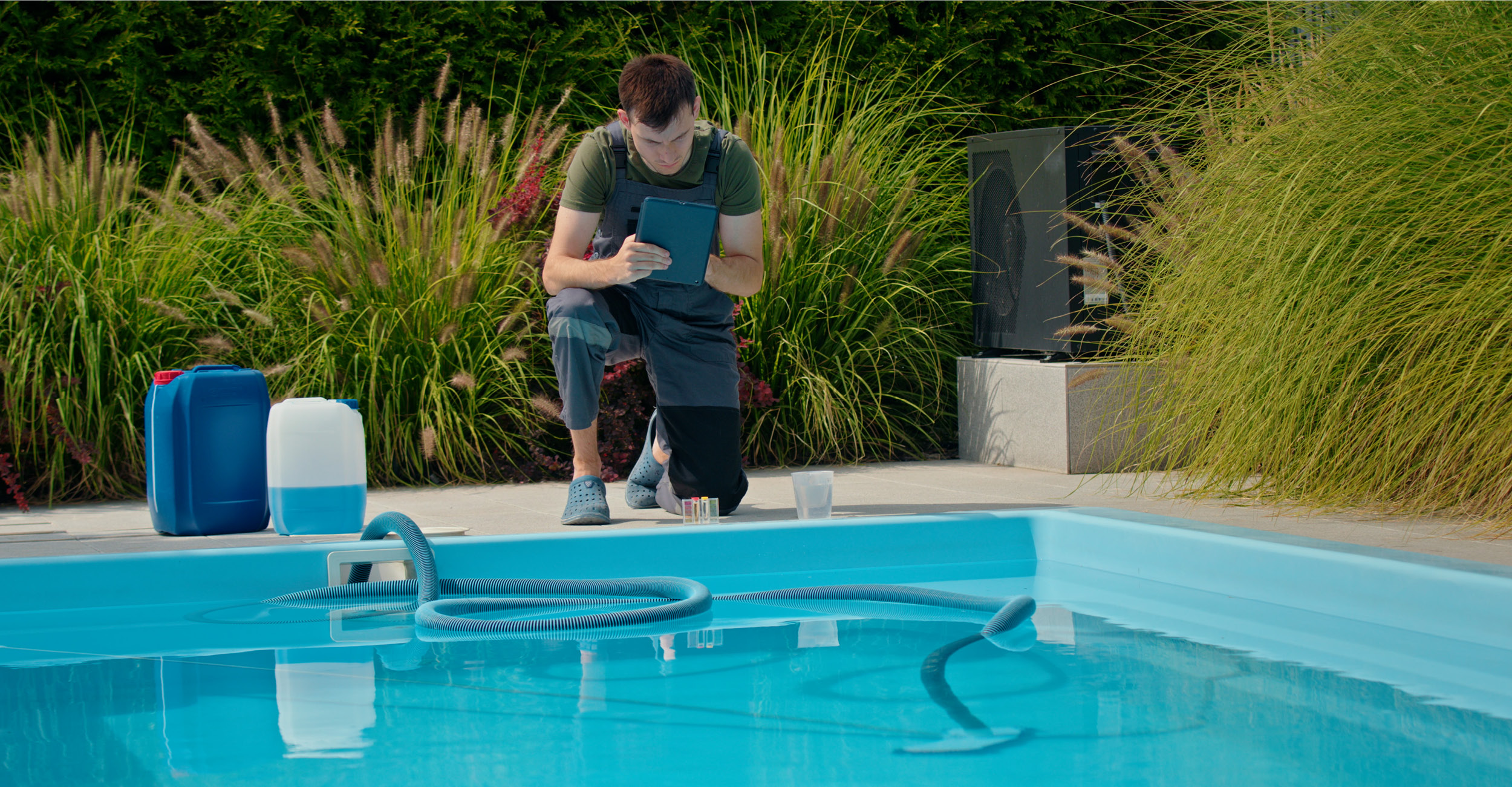 Homme professionnel testant la qualité de l'eau dans une piscine coque moderne entourée de verdure, illustrant un entretien méticuleux avec des produits chimiques, soulignant l'expertise en maintenance de piscines.