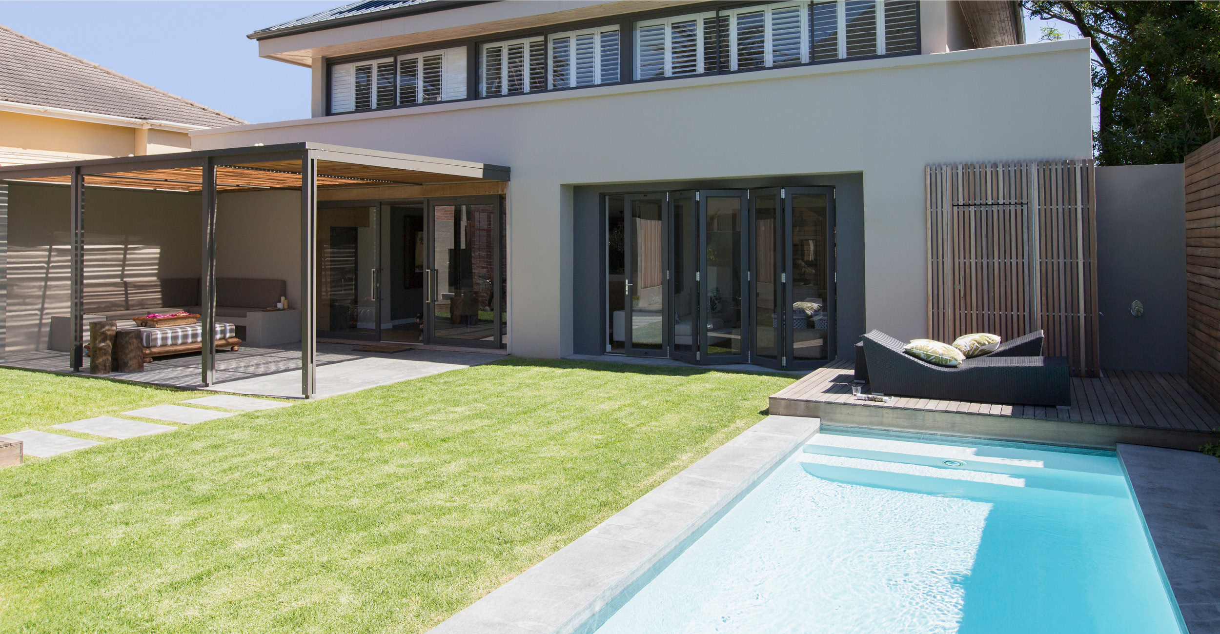 Espace extérieur moderne avec piscine coque intégrée, entourée d'un aménagement paysager soigné et d'une terrasse contemporaine, alliant des matériaux de bois et métal, offrant une ambiance chaleureuse et élégante idéale pour la détente.