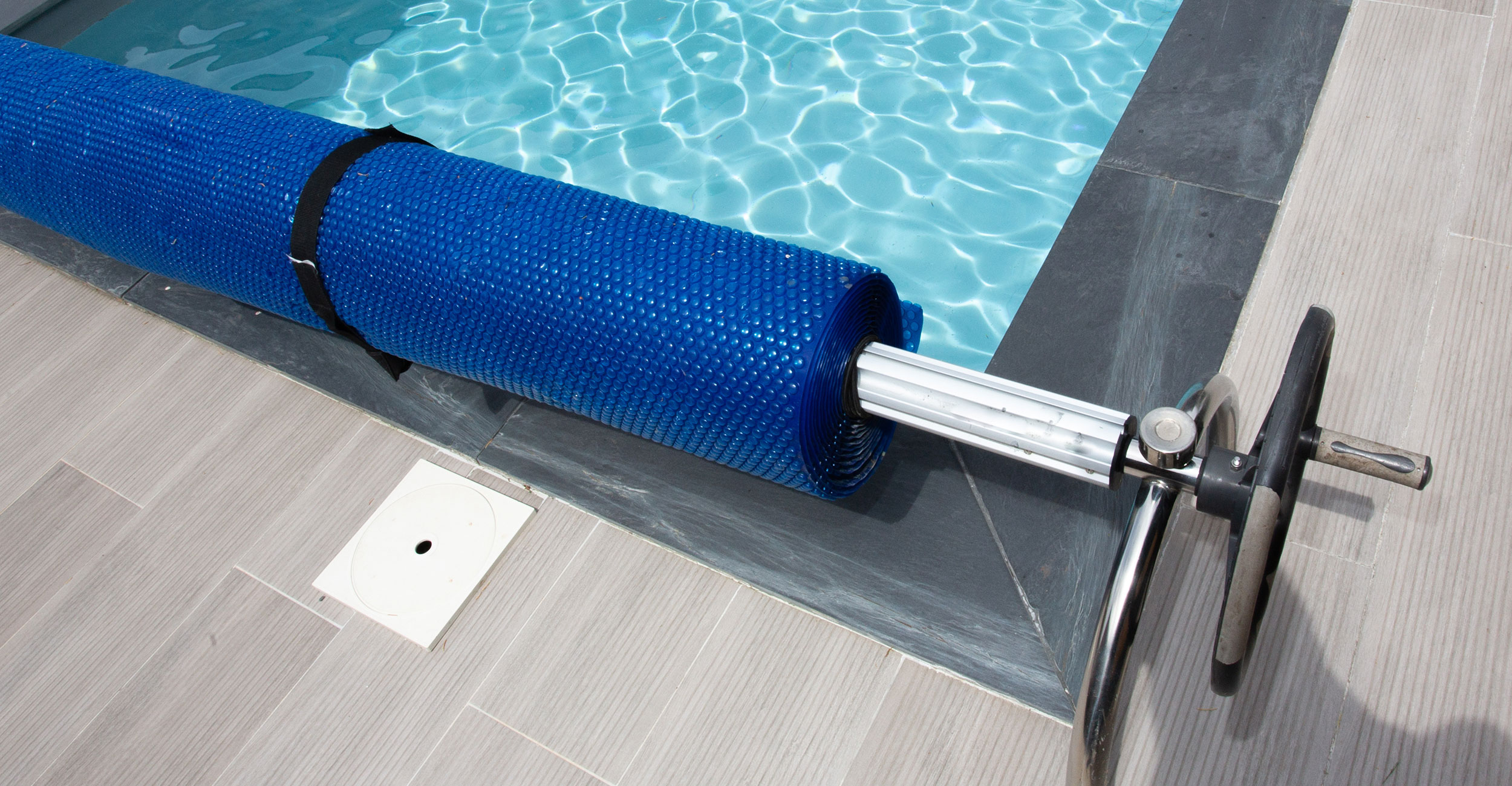 Enrouleur de bâche pour piscine coque avec structure en acier inoxydable sur carrelage moderne, accessoire essentiel pour faciliter l'entretien d'une piscine propre et élégante