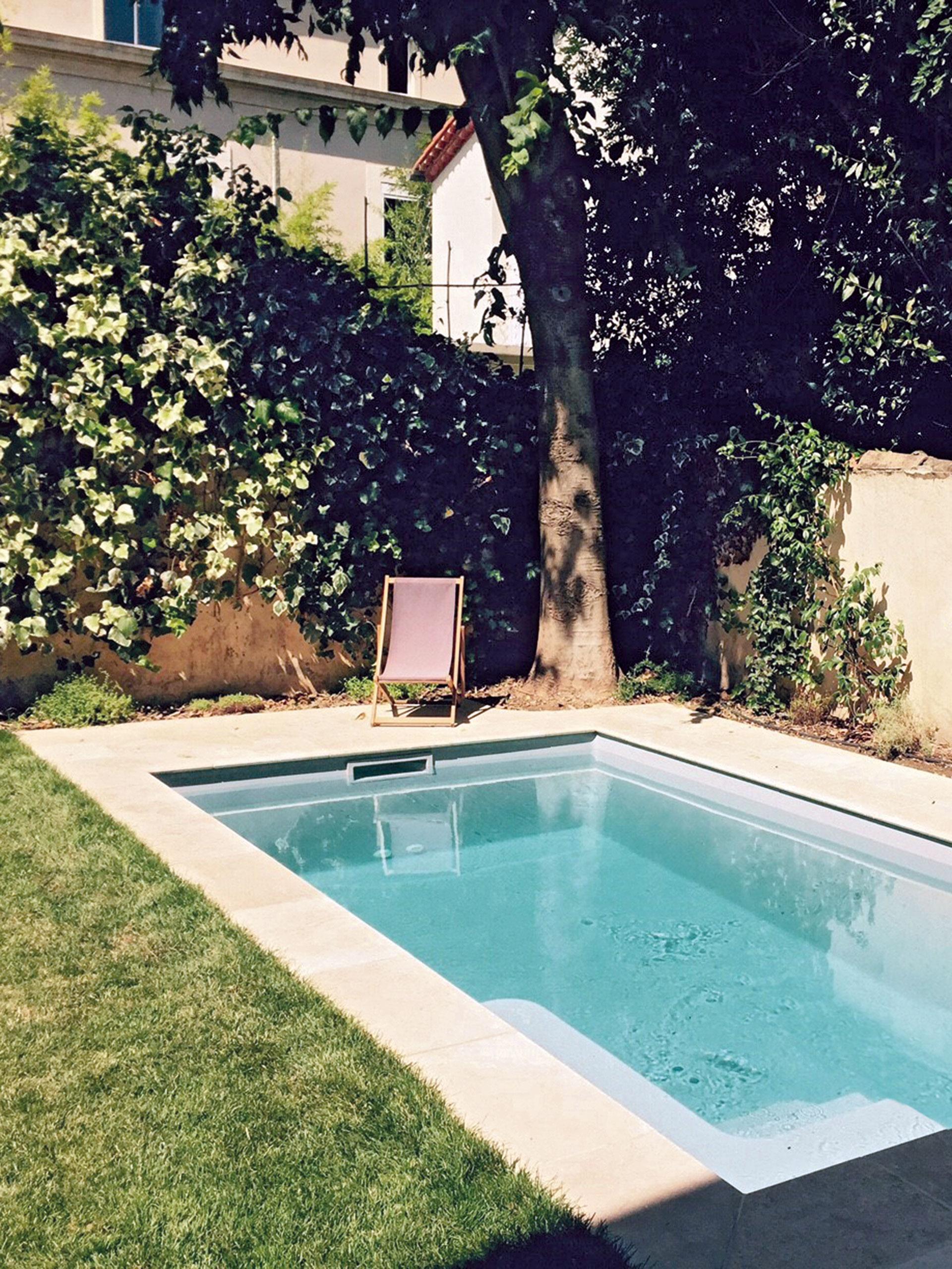 Espace extérieur moderne avec piscine coque rectangulaire entourée de béton clair, végétation luxuriante et mobilier de jardin, idéale pour détente et loisirs en famille.