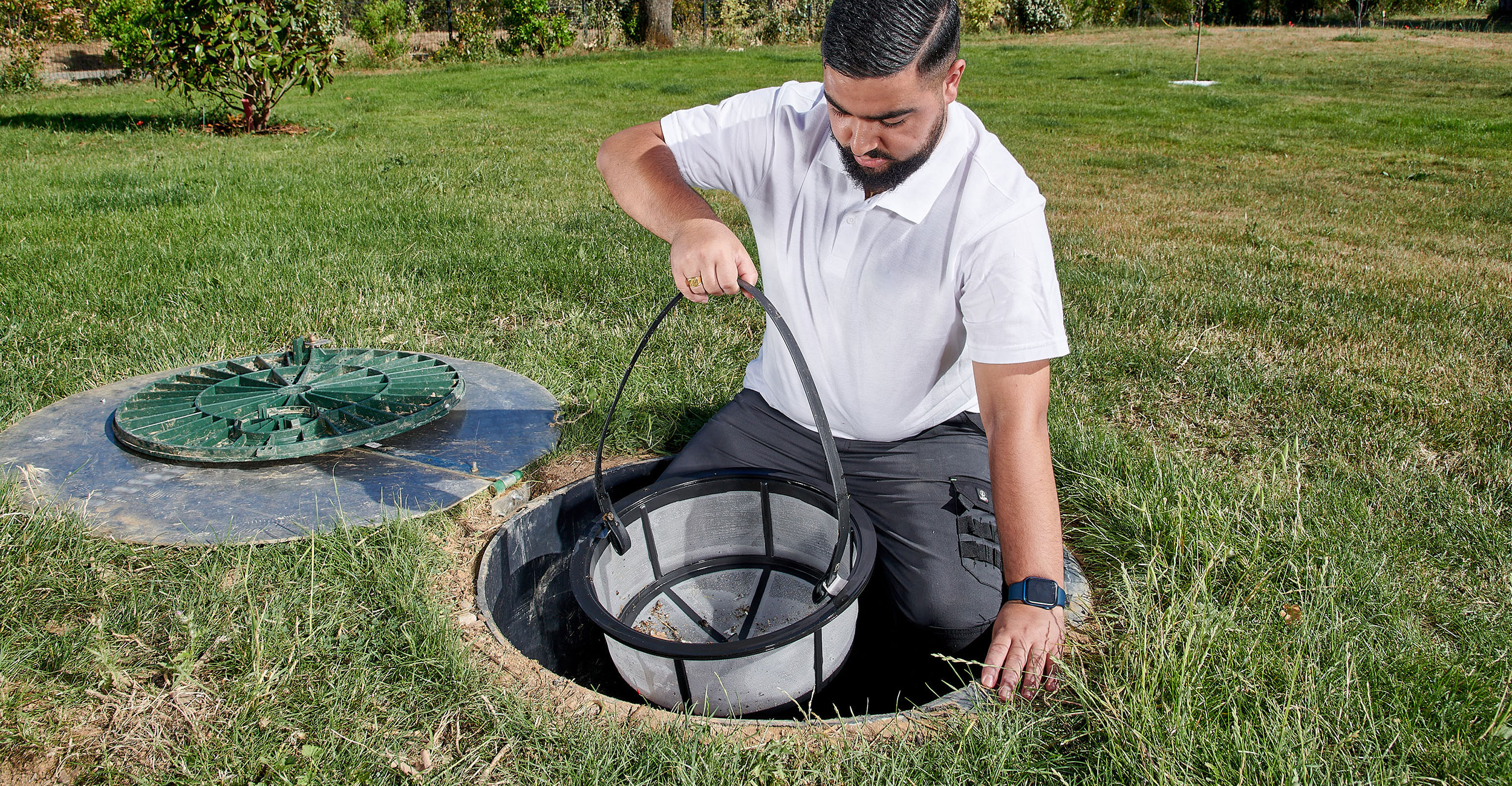 Expert en maintenance de piscine coque vérifiant le système de filtration avec attention, extérieur soigné avec gazon et plantes reflétant professionnalisme et propreté